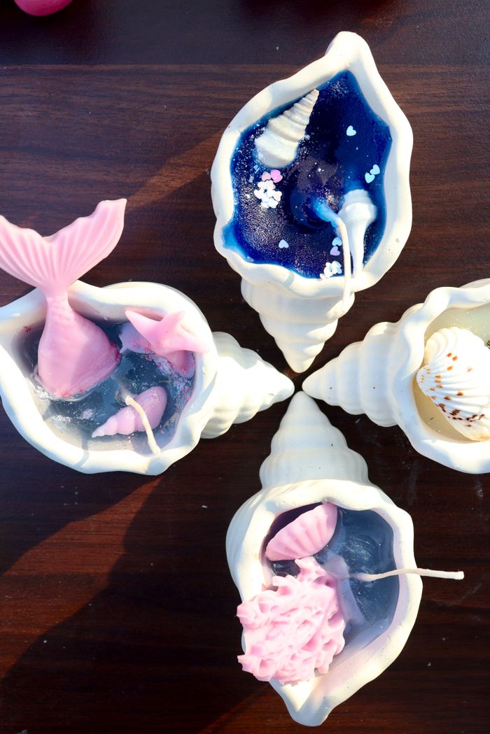 Four shell-shaped candles with ocean-inspired designs on a wooden surface.